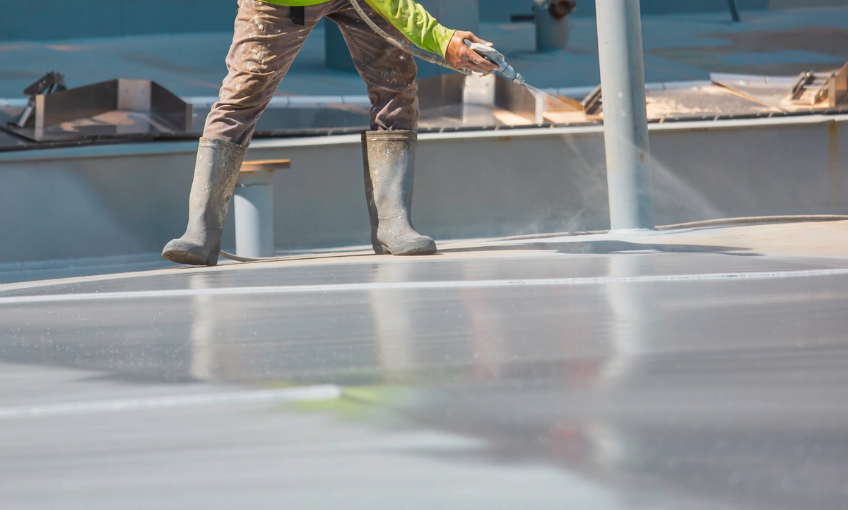 Commercial roof worker sprays flat roof with an industrial coating