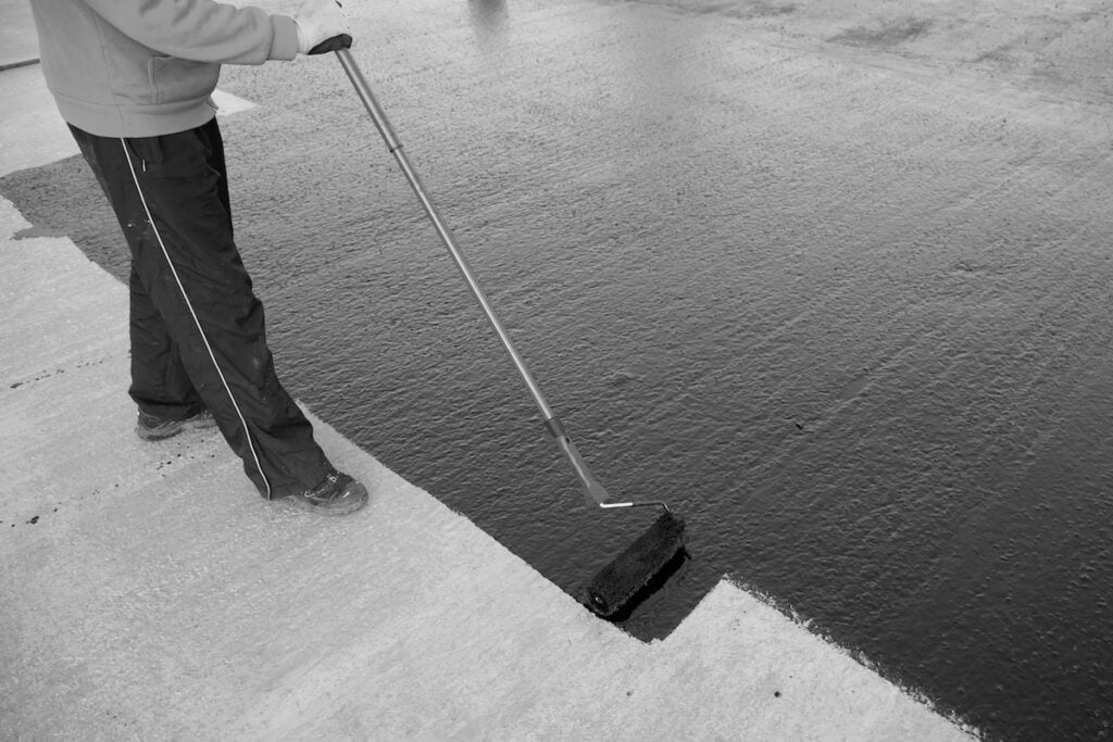 Waterproofing coating. Worker applies bitumen with a roller brush.