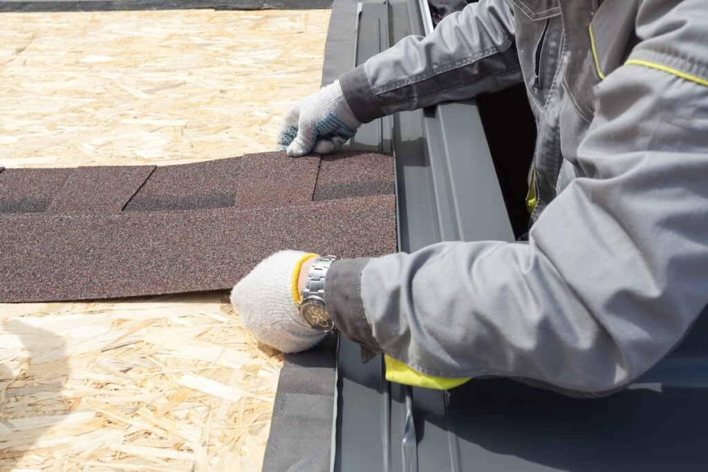 professional roofer worker lays asphalt sheet on the rooftop, holding roof tile in hands