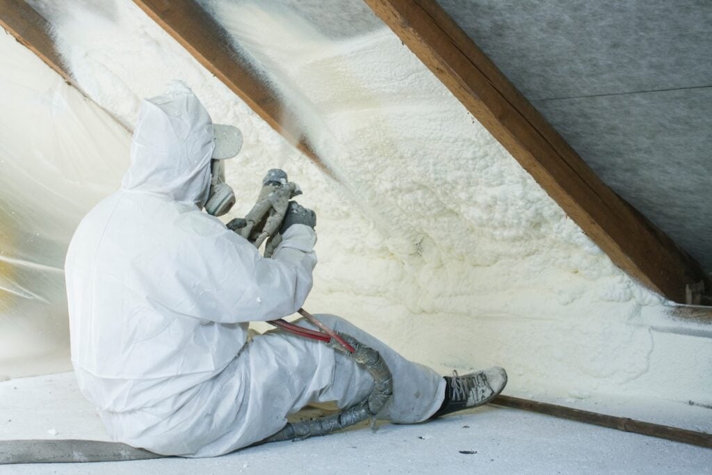 spray polyurethane foam for roof - technician spraying foam insulation using plural component gun for polyurethane foam