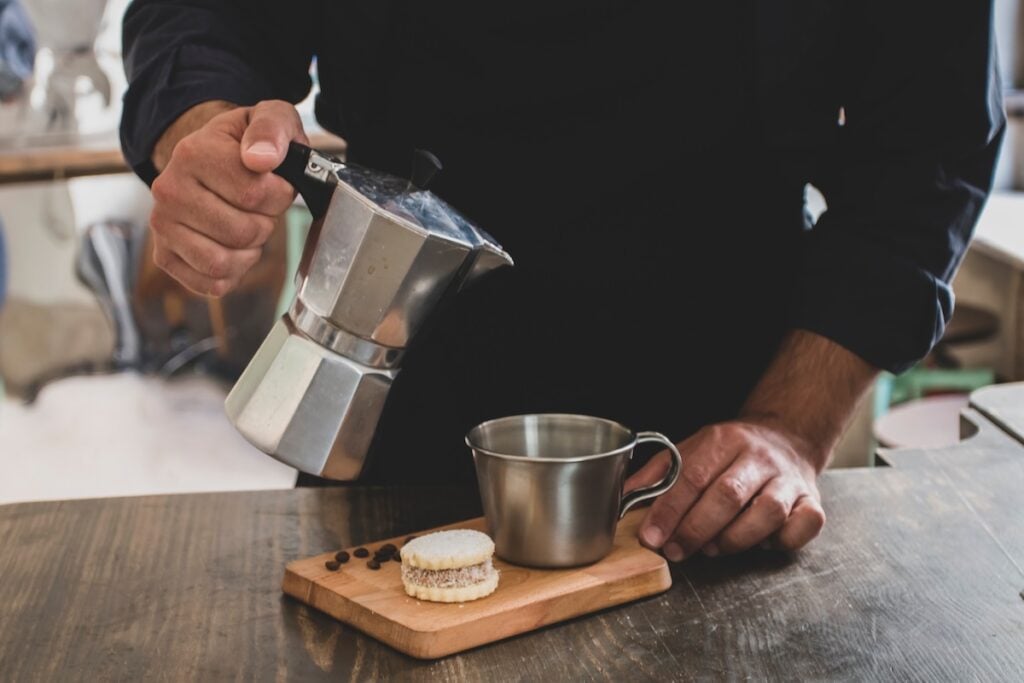 Male Barista preparing fresh espresso in coffee maker for customer in a coffee shop. 
