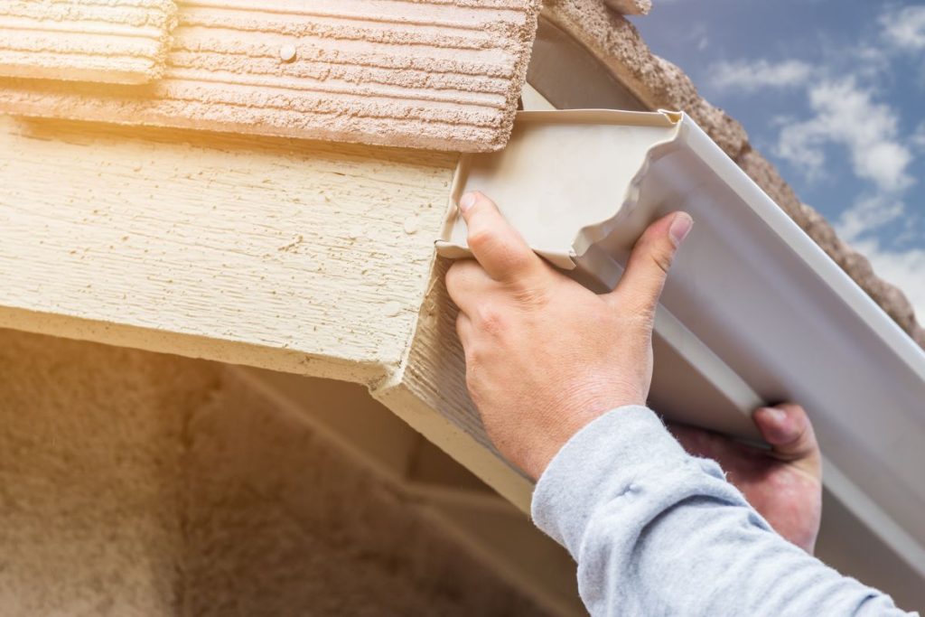 Hands installing aluminum rain gutter to fascia of house