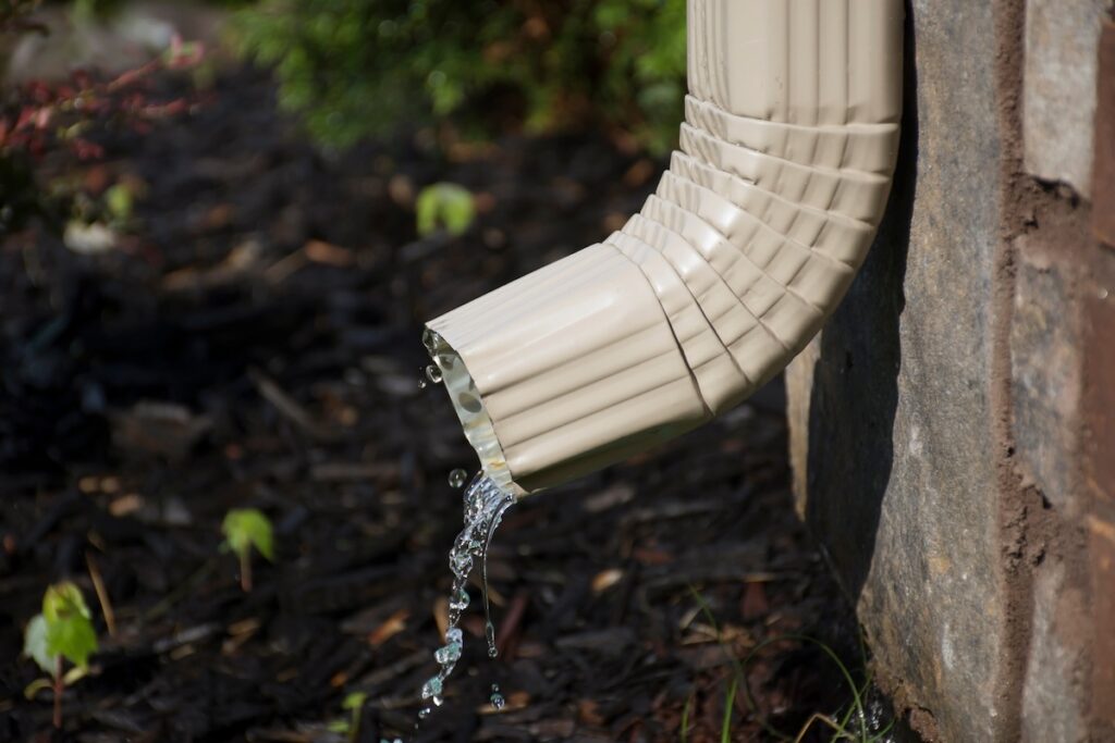 A rain gutter downspout with water coming out from the side